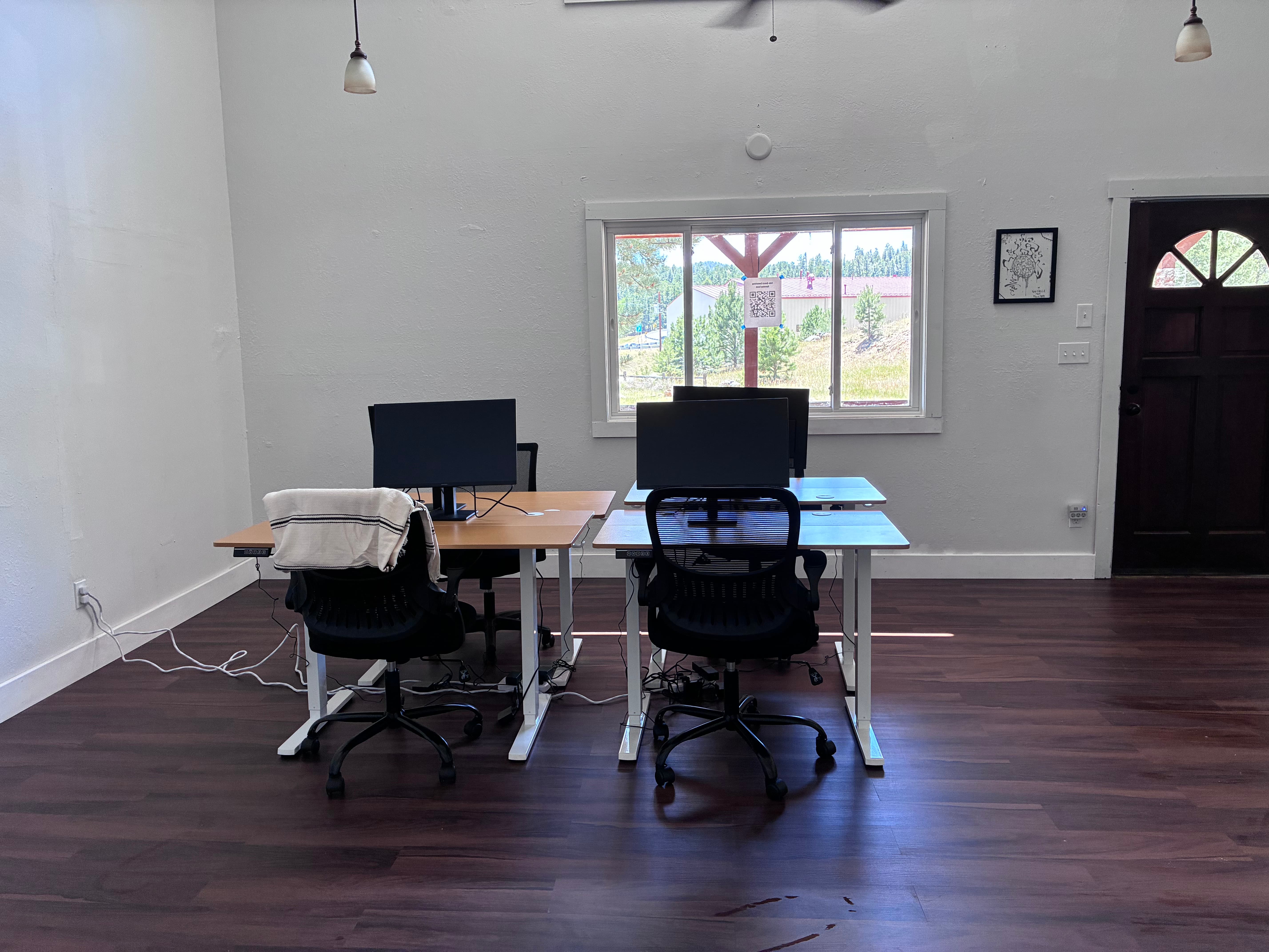 Open coworking floor with four stand-up desks, ergonomic chairs, and hillside views